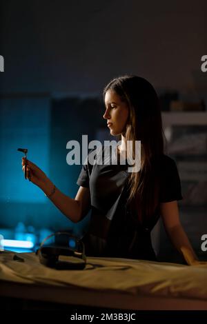 Porträt einer jungen brünetten Frau in schwarzer medizinischer Uniform. Eine Ärztin im Hals-Nasen-Ohren-Bereich hält ein Gerät zur Untersuchung kranker Patienten in den Händen. Stockfoto