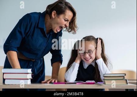 Eine Lehrerin schreit eine Schülerin an. Das kleine Mädchen bedeckt ihre Ohren mit den Händen. Stockfoto