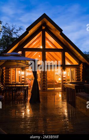 Blockhütte im A-Rahmen-Stil mit verwässerter Holzterrasse in der Dämmerung im Sommer. Stockfoto