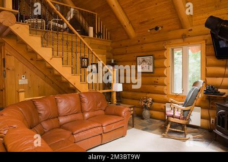 Dunkles braunes Ledersofa im Wohnzimmer und Treppe führt zum Hauptschlafzimmer oben in der Blockhütte. Stockfoto