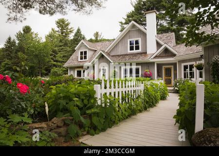 New Hampton Cottage-Stil Haus mit landschaftlich gestaltetem Vorgarten und Holzsteg im Sommer, Quebec, Kanada. Dieses Bild ist Eigentum freigegeben. CUPR0208 Stockfoto