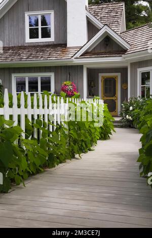 Haus im Hampton Cottage-Stil mit landschaftlich gestaltetem Vorgarten und Holzsteg im Sommer, Quebec, Kanada. Dieses Bild ist Eigentum freigegeben. CUPR0208 Stockfoto