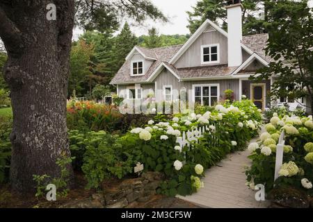 New Hampton Cottage-Stil Haus mit landschaftlich gestaltetem Vorgarten und Holzsteg im Sommer, Quebec, Kanada. Dieses Bild ist Eigentum freigegeben. CUPR0208 Stockfoto