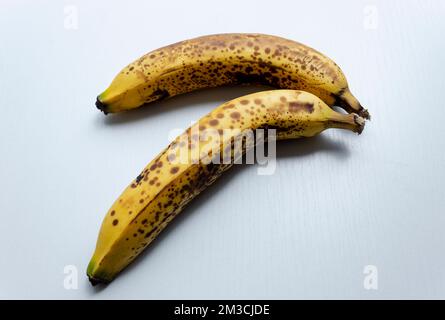 Nahaufnahme zu zwei gelben Sommersprossen Bananen in diagonaler Form über einem weißen Holztisch. Stockfoto
