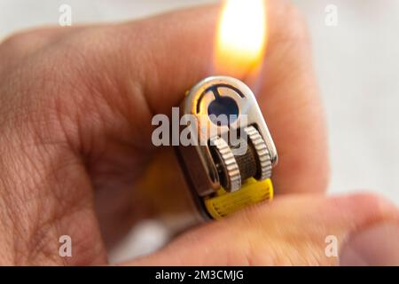 Nahaufnahme zu einer männlichen Hand, die ein gelbes Feuerzeug mit Flamme auf weißem Hintergrund hält Stockfoto
