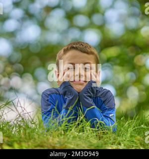 Ein Porträt eines jungen, glücklichen Jungen in einem grünen Park, in tiefer Überlegung. Stockfoto