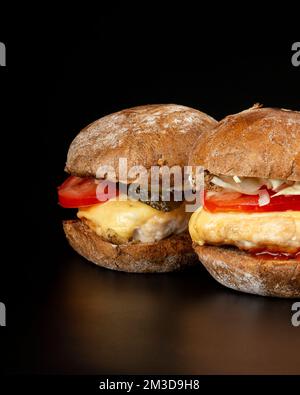 2 saftige Burger mit Gemüse und ein großes Hähnchenschnitzel im dunklen Hintergrund, Fast Food Cheeseburger. Stockfoto