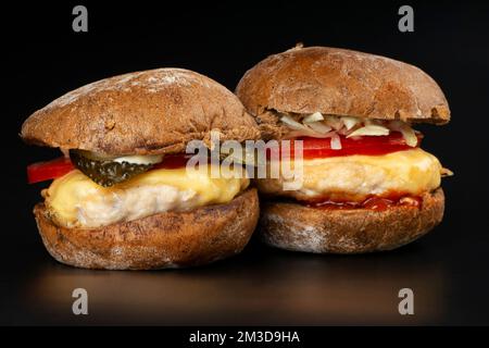 2 saftige Burger mit Gemüse und ein großes Hähnchenschnitzel im dunklen Hintergrund, Fast Food Cheeseburger. Stockfoto