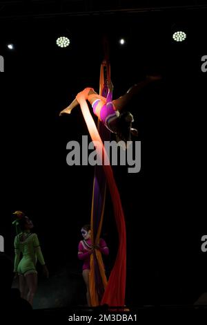 Ein professioneller Zirkuskünstler auf roter, leuchtender Luftseide sorgt für ein ausgewogenes Gleichgewicht auf einem Spalt Stockfoto