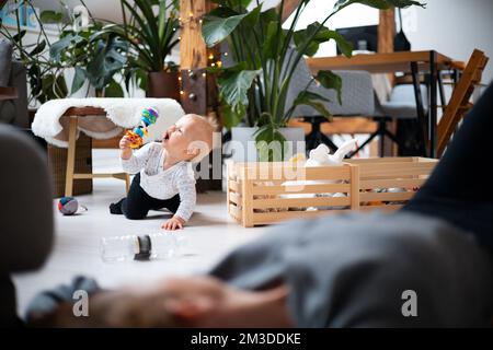 Glückliche Familienmomente. Die Mutter liegt bequem auf der Kindermatte und sieht ihrem Baby im Wohnzimmer die Spielchen an. Positive menschliche Emotionen, Gefühle, Freude. Stockfoto