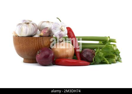 Zwiebeln, Chili und Knoblauchzwiebeln in Holzschüssel vor frischem Sellerie-Stiel, Gewürzen oder Gewürzmotiven Stillleben isoliert auf weißem Hintergrund Stockfoto