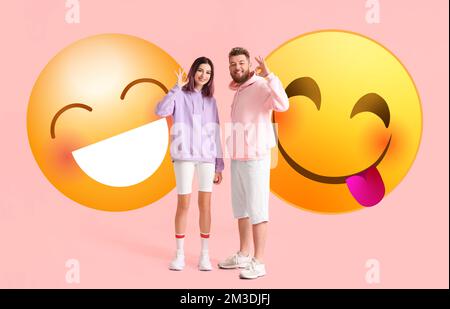 Cooles junges Paar in Hoodies und großen lächelnden Emoticons auf pinkfarbenem Hintergrund Stockfoto
