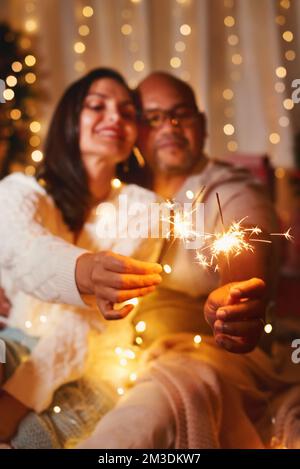 Fröhliche interrassische Kaukasierin, afroamerikanisches schwarzes Paar, Frau und Mann, die sich amüsieren, mit bengalischen Lichtern zu Hause, um Silvester-Weihnachten zu feiern. Ha Stockfoto