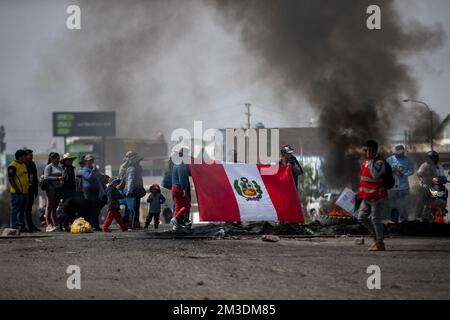 Arequipa, Peru. 14.. Dezember 2022. Demonstranten protestieren auf einer Straße neben brennenden Reifen und halten eine peruanische Flagge hoch. Die Regierung in Peru hat angesichts der immer heftigeren Proteste gegen den Sturz von Präsident Castillo im ganzen Land den Notstand ausgerufen. Kredit: Denis Mayhua/dpa/Alamy Live News Stockfoto