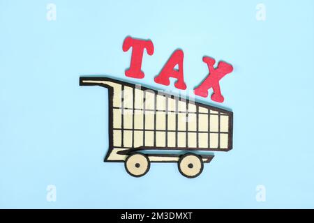 Einkaufs-, Verkaufs- und Verbrauchersteuerkonzept. Hölzerner Einkaufswagen mit Wort auf blauem Hintergrund. Stockfoto