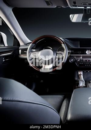Dunkler Luxus-Innenraum – Lenkrad, Schalthebel und Armaturenbrett. Das Auto ist drin. Beige bequeme Sitze, Lenkrad, Armaturenbrett, Klimaregelung, Stockfoto