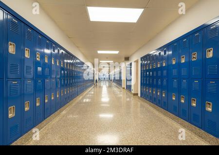Typischer, unscheinbarer, in den USA leerer Schulflur mit blauen Metallschließfächern entlang eines Flurs. Stockfoto