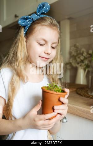 Kleines Mädchen in ihrer Küche sitzt und hält einen Topf mit Sämlingen Stockfoto