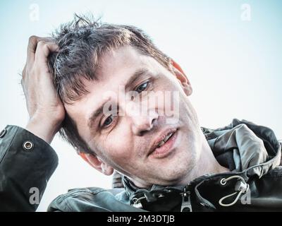 Ein lustiger, positiver, junger Träumer, der seinen Kopf in der Hand hält und denkt. Stockfoto