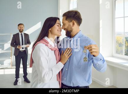 Ein verliebtes Paar umarmt seine neue Wohnung und hält Schlüssel in der Hand, nachdem es Immobilien gekauft hat. Stockfoto