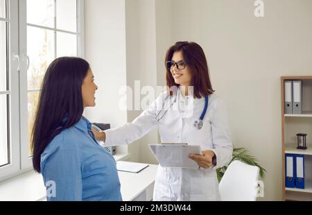 Glückliche Arzthelferin zur Unterstützung einer lächelnden Patientin in der Klinik Stockfoto