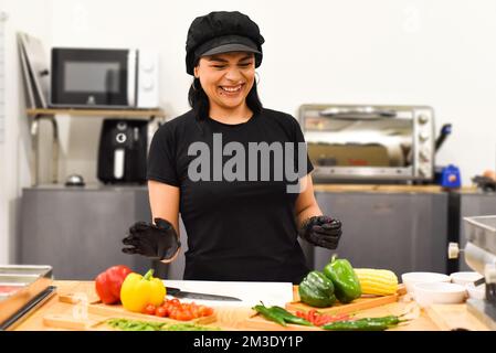 Eine Mexikanerin, die lacht, während sie Tacos in der Küche kocht Stockfoto