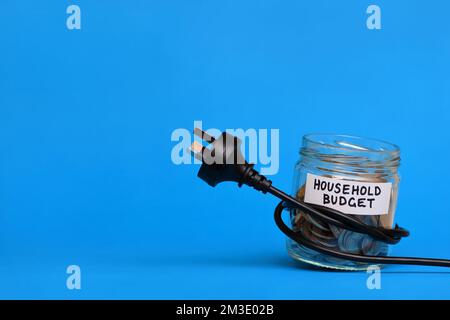 Ein konzeptionelles Bild eines Stromkabels, das um ein Glas Geld gewickelt ist und symbolisiert, wie die Haushaltsbudgets durch die Strompreise erdrosselt werden Stockfoto