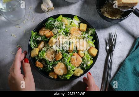 Nahaufnahme einer Frau, die Cesar-Salat mit Gabel auf einem grauen Marmortisch isst Stockfoto