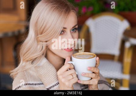 Portrait hübsche blonde Frau, lächelnde Frau in gemütlichem Karo, sitzt im Café mit einer Tasse heißem Kaffee, freut sich an einem glücklichen Morgen Stockfoto