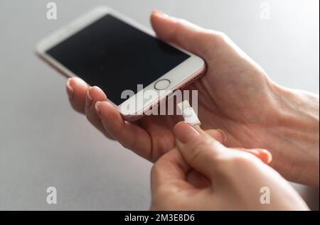 Smartphone wird auf weißem Hintergrund per Hand aufgeladen. Blick von oben. Laden Sie Ihr Telefon auf. Stockfoto