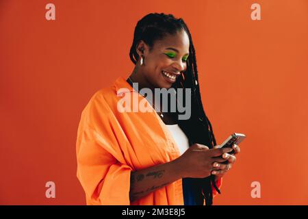 Frau in Freizeitkleidung, die ein Smartphone in einem Studio benutzt. Glückliche junge Frau, die gerne soziale Medien nutzt. Stockfoto