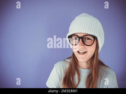 Ein junges Mädchen mit dicken, massiven Gläsern und Beanie vor lila Hintergrund Stockfoto