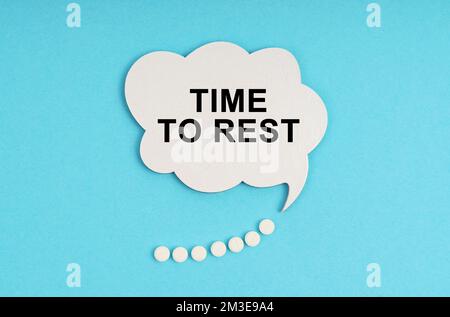 Medizin und Gesundheitskonzept. Auf einem blauen Tisch sind Pillen und ein weißer Teller mit der Inschrift - Zeit zum Ausruhen Stockfoto