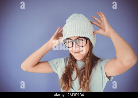 Ein junges Mädchen mit dicken, massiven Gläsern und Beanie vor lila Hintergrund Stockfoto