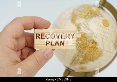 Globalisierungskonzept. Ein Mann hält in der Hand eine Holzplatte, auf der es steht - EIN WIEDERAUFFÜLLUNGSPLAN. Im Hintergrund ist ein Globus. Stockfoto