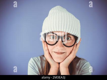 Ein junges Mädchen mit dicken, massiven Gläsern und Beanie vor lila Hintergrund Stockfoto