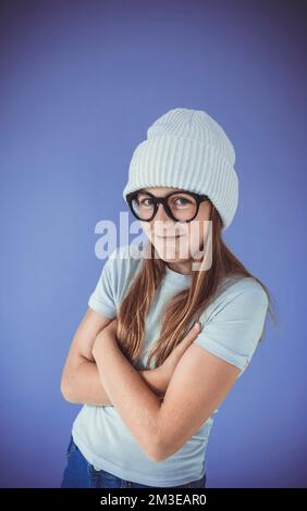 Ein junges Mädchen mit dicken, massiven Gläsern und Beanie vor lila Hintergrund Stockfoto