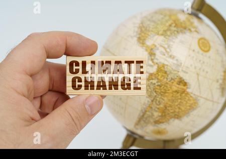 Globalisierungskonzept. Ein Mann hält in seiner Hand eine Holzplatte, auf der es steht - Klimawandel. Im Hintergrund ist ein Globus. Stockfoto