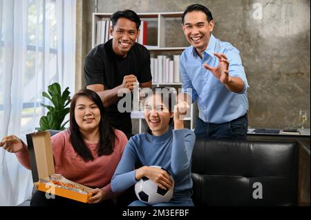 Eine Gruppe fröhlicher und aufgeregter asiatischer Freunde sitzt auf dem Sofa und schaut Fußball oder Fußballmannschaft zusammen im Fernsehen an und jubelt sie an. Sport- und Unterhaltungskonzept Stockfoto
