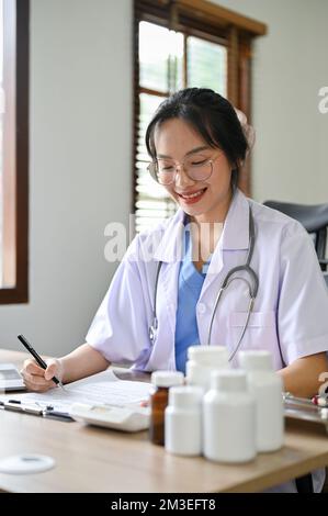 Porträt, professionelle Millenialärztin oder Apothekerin in weißem Kleid, die an ihrem Schreibtisch in der Klinik arbeitet. Stockfoto