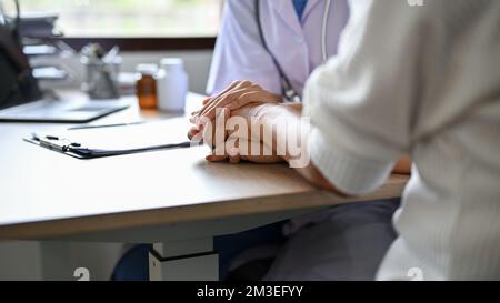 Nahaufnahme: Eine Ärztin hält die Hände des Patienten auf dem Tisch, während sie den Behandlungsplan bespricht. Stockfoto