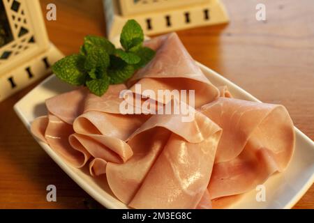 Dünne Scheiben Yorker Schinken auf einem kleinen weißen Tablett mit kleinen Minzblättern für Farbe und Aroma Stockfoto