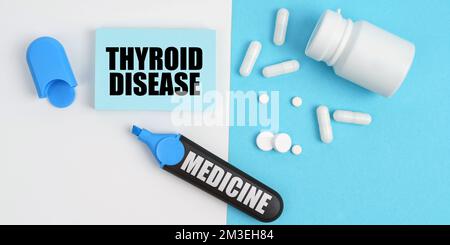 Medizinisches Konzept. Auf der weißen und blauen Oberfläche sind Pillen, ein Marker und Papier mit der Inschrift - Schilddrüsenerkrankung Stockfoto