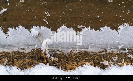 Spitzenmuster der gefrorenen Wasserkante am Teich Stockfoto
