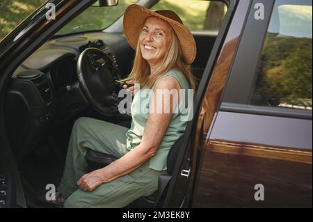 Aufgeregte ältere Frau, die im neuen Auto im Freien sitzt und die Schlüssel hält, lächelt und das neu gekaufte Auto genießt. Fahrkurse, Versicherung, Autoreise. Aktivität im Ruhestand. Glückliche Kundin Autohaus Stockfoto