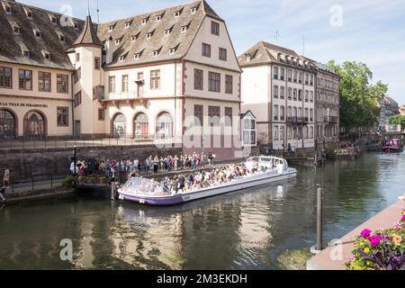 Touristen in einem Ausflugsboot im alten Zollhaus auf dem Fluss Ill an einem sonnigen Tag in Straßburg, Frankreich. Jetzt ist es ein Bauernmarkt namens La Nouvelle Douane. Stockfoto