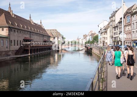 An einem sonnigen Tag in Straßburg, Frankreich, gehen die Menschen am ehemaligen Zollhaus auf dem Fluss Ill vorbei. Jetzt ist es ein Bauernmarkt namens La Nouvelle Douane. Stockfoto