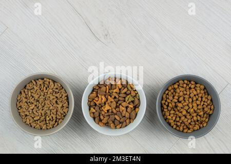 Trockenfutter für Katzen und Hunde in Schalen auf weißem Holzhintergrund. Draufsicht. Stockfoto