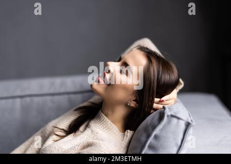 Ruhiges, zufriedenes Mädchen, das sich auf der Couch ausstreckt und an einen angenehmen, faulen Tag denkt, träumt und sonntagmorgen plant Stockfoto