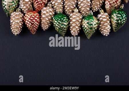 Weihnachtsdekorationen in Form von rot-grünen und goldenen Kiefernzapfen mit Platz für Text auf schwarzem Hintergrund Stockfoto